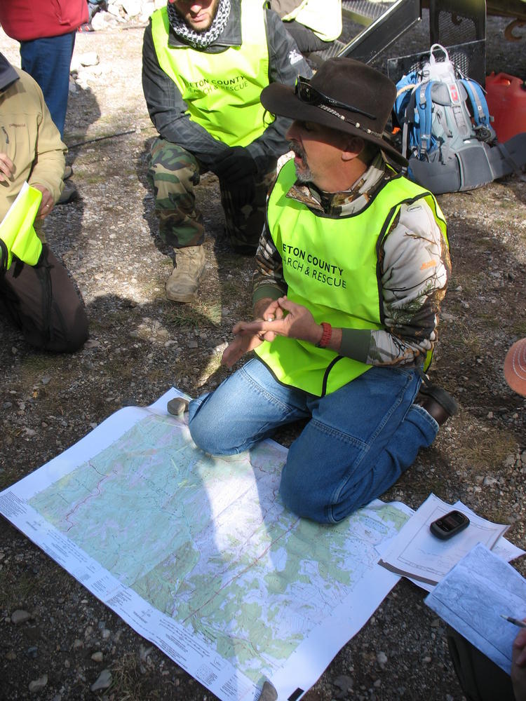 Man kneeling on the ground over a map, talking to others around him