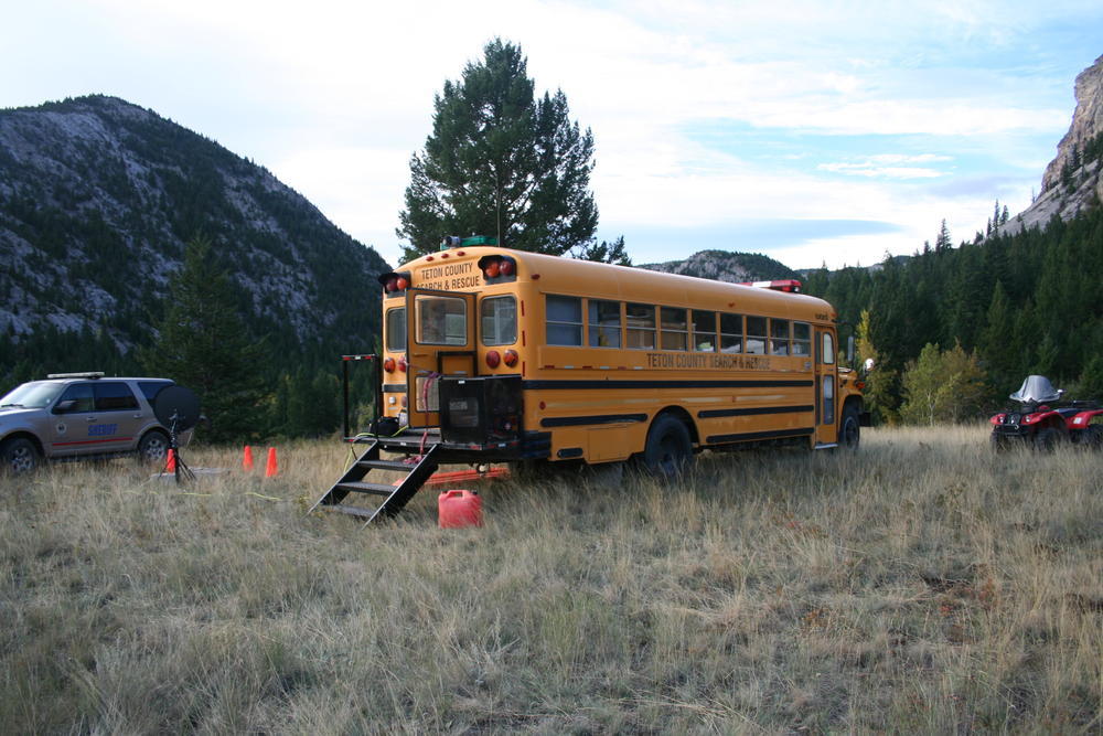 school bus parked in a grassy field with stairs coming out of the back door, sheriff's office vehicle parked next to it