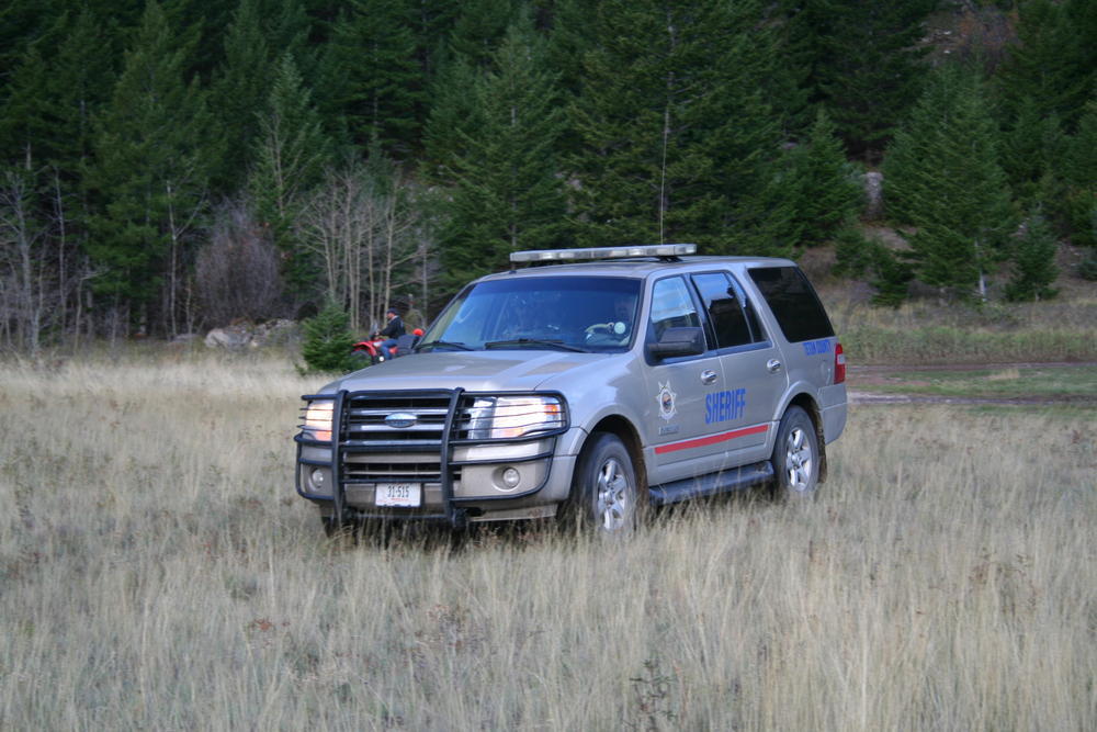 sheriff's office vehicle parked in a grassy field with a fourwheeler behind it